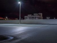 a parking lot is illuminated with street lamps by a tall white building in the city