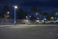 a dark parking lot with several lights over it and a chain link fence to the side