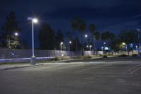 a dark parking lot with several lights over it and a chain link fence to the side