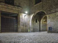 the street is very dark and empty, with a light on a stone floor and a wall