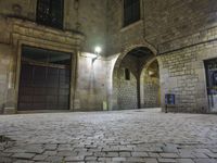 the street is very dark and empty, with a light on a stone floor and a wall