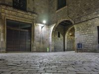 the street is very dark and empty, with a light on a stone floor and a wall