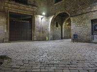 the street is very dark and empty, with a light on a stone floor and a wall