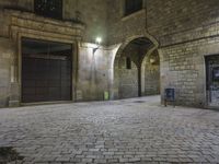 the street is very dark and empty, with a light on a stone floor and a wall