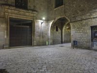 the street is very dark and empty, with a light on a stone floor and a wall