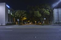 a dark street at night with trees and stoplights on it's side by a building