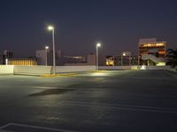 an empty parking lot is lit up at night with bright street lights overhead them are buildings and palm trees