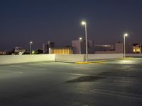 an empty parking lot is lit up at night with bright street lights overhead them are buildings and palm trees