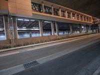 the side of a large long building with windows at night time outside, along an empty city street