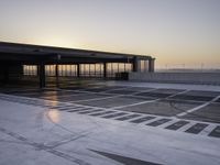 an airport parking area with the sun setting in the sky behind it, overcast