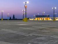 parking lot at dusk with several traffic lights next to it and multiple cars parked in front of the building