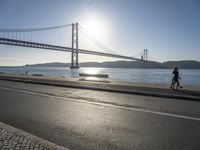 a person is running and riding on the street near the water below the bridge in the evening