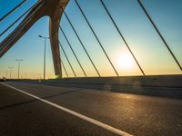 a view of the sun setting over the bridge from the bike path with it's headlights shining on a sunny day