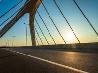 a view of the sun setting over the bridge from the bike path with it's headlights shining on a sunny day