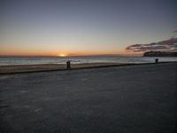 the man is walking on the edge of a road near the beach as the sun sets