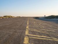 an empty parking lot near the beach and grassy grass at sunset time with the sand dunes up side