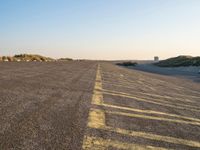 an empty parking lot near the beach and grassy grass at sunset time with the sand dunes up side