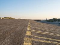 an empty parking lot near the beach and grassy grass at sunset time with the sand dunes up side