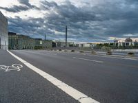 a person riding their bicycle along the street, by a building with a cloudy sky