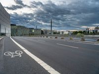 a person riding their bicycle along the street, by a building with a cloudy sky