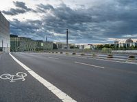 a person riding their bicycle along the street, by a building with a cloudy sky