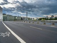 a person riding their bicycle along the street, by a building with a cloudy sky