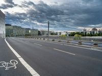 a person riding their bicycle along the street, by a building with a cloudy sky