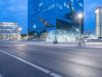 bike and car driving in the evening in front of a modern office building with glass windows