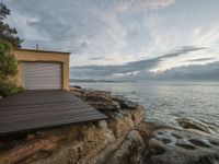 an open wooden deck overlooking the water in front of a beach cottage and garage building