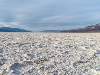 white sand in middle of desert area, desert mountains in the background with rocks scattered across the area