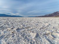 white sand in middle of desert area, desert mountains in the background with rocks scattered across the area