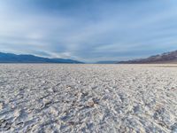 white sand in middle of desert area, desert mountains in the background with rocks scattered across the area