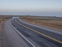 a large asphalt road leading into the distance by the ocean and an airplane is flying