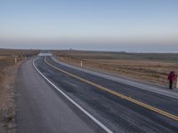 a large asphalt road leading into the distance by the ocean and an airplane is flying