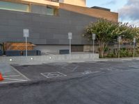 a building with a few parking spaces marked out in the concrete with street signs, and a cone in the street