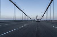 three vehicles driving over a bridge near the ocean in the sunset, and at the opposite time a person is crossing