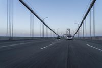 three vehicles driving over a bridge near the ocean in the sunset, and at the opposite time a person is crossing