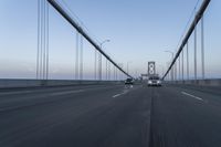 three vehicles driving over a bridge near the ocean in the sunset, and at the opposite time a person is crossing