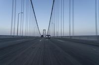 a car drives across the bridge as another is in the distance as the sky begins to blue