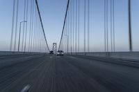 a car drives across the bridge as another is in the distance as the sky begins to blue