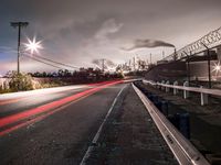 a long exposure photograph of cars going under power lines near an industrial site with smoke coming from chimneys