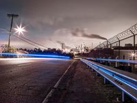 a long exposure photograph of cars going under power lines near an industrial site with smoke coming from chimneys