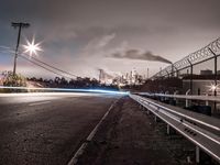 a long exposure photograph of cars going under power lines near an industrial site with smoke coming from chimneys