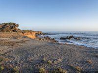 a grassy field by the shore and a cliff with rocks in the ocean in the background