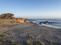 a grassy field by the shore and a cliff with rocks in the ocean in the background