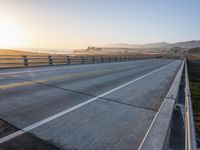 a paved highway with yellow lines and traffic on both sides and hills behind it as the sun goes down