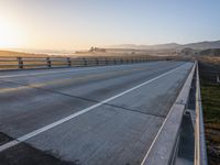 a paved highway with yellow lines and traffic on both sides and hills behind it as the sun goes down