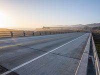 a paved highway with yellow lines and traffic on both sides and hills behind it as the sun goes down