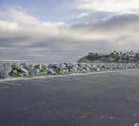 a parking lot that has rocks by the ocean on it and trees in the background