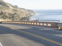 the man is riding his motorcycle on the side of the road beside a cliff overlooking the ocean